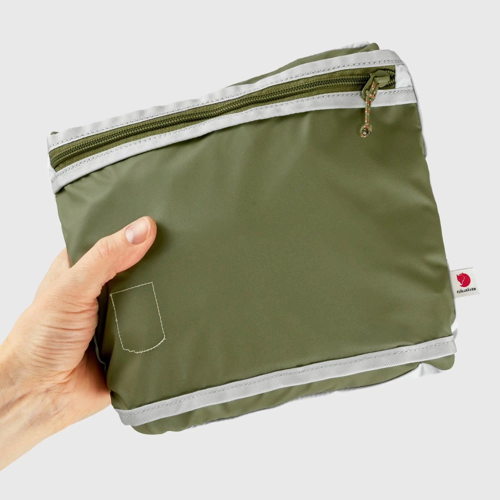 Fjallraven High Coast Totepack, pack folded into its pocket and held in one hand, shown in Green; shared feature image
