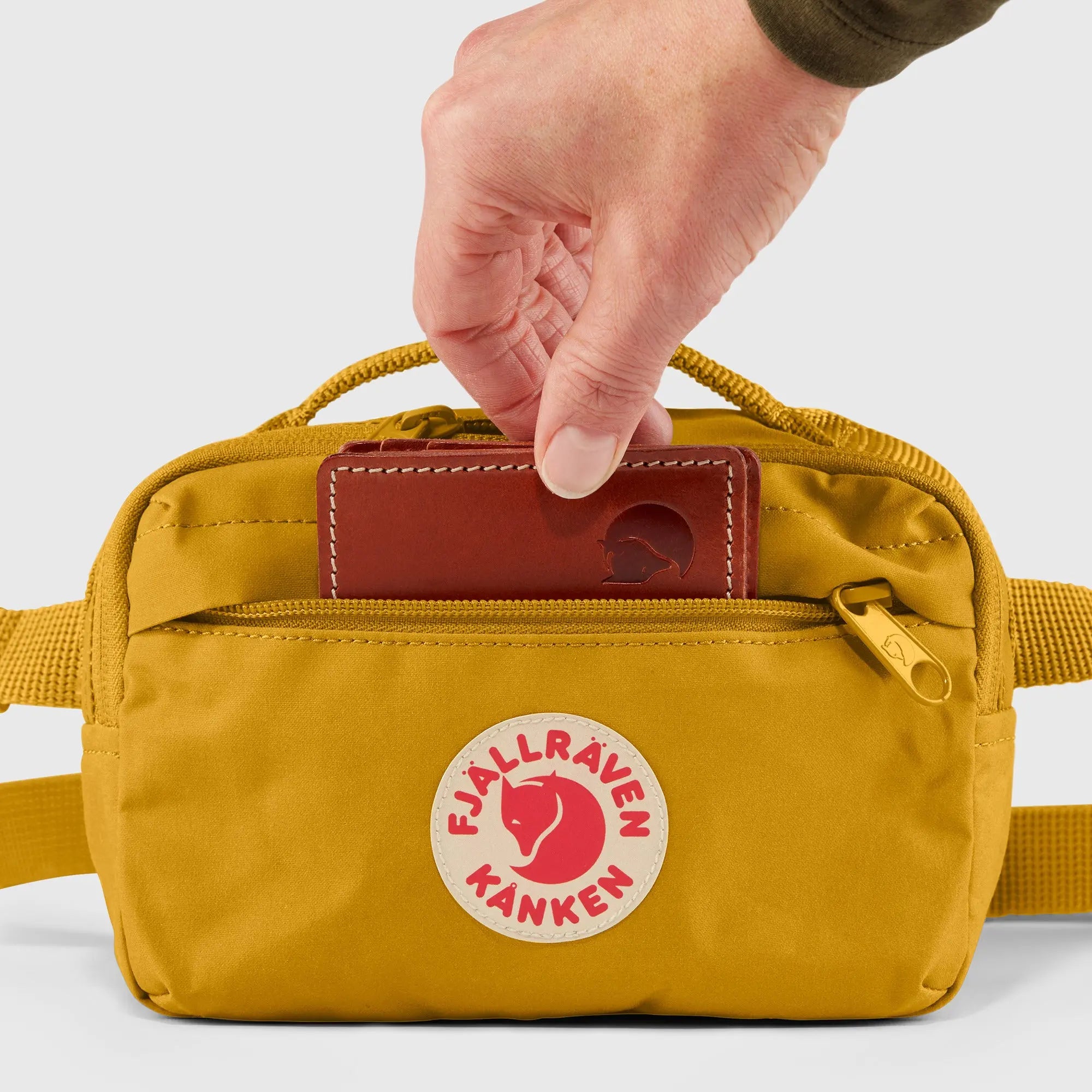 Fjallraven Kanken Hip Pack, front pocket holding a wallet, shown in Ochre; shared feature image