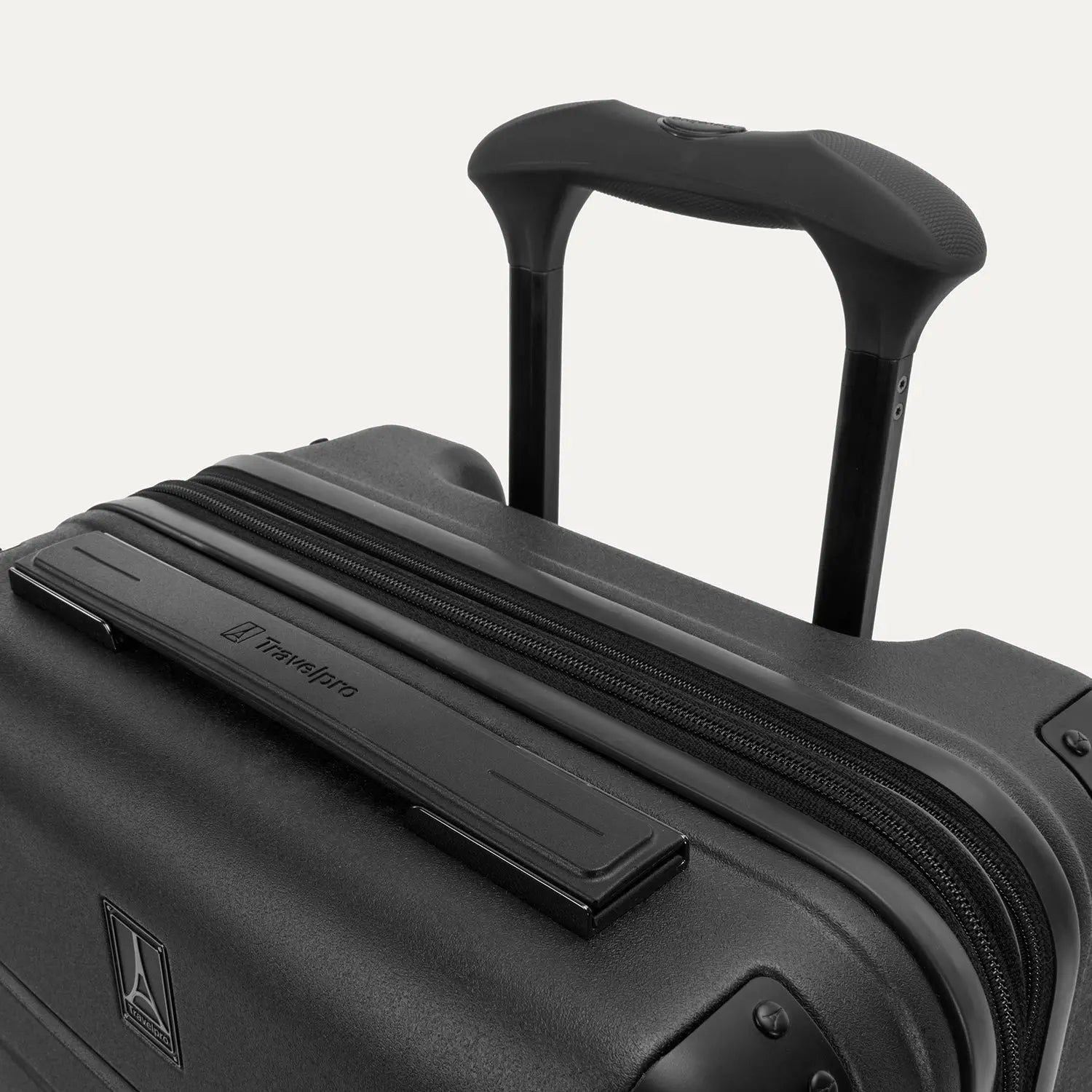Close-up detail of the Travelpro Platinum Elite Compact Carry-On Hardside Spinner in Shadow Black, showing the low-profile top carry handle with the Travelpro logo and the sturdy PowerScope Lite telescoping handle.