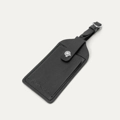 Close-up of the premium black leather luggage tag with the embossed Travelpro logo, featuring a secure buckle strap and a privacy flap for contact information.