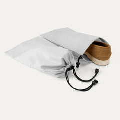 detail view of the two removable gray shoe bags included with the travelpro platinum elite compact carry-on hardside spinner in aviator navy, shown with a brown suede loafer being tucked inside for organized packing.
