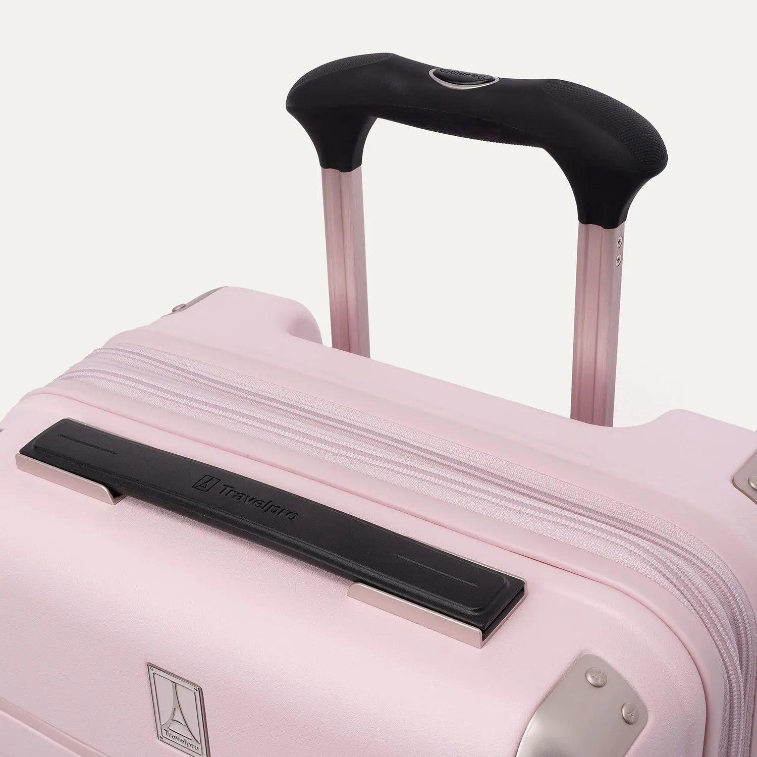 Close-up view of the light pink Travelpro Platinum Elite Next Gen Powder Pink Suitcase, highlighting the black ProGrip telescoping handle, top carry handle, metallic corner guards, and Travelpro logo badge against an off-white background.