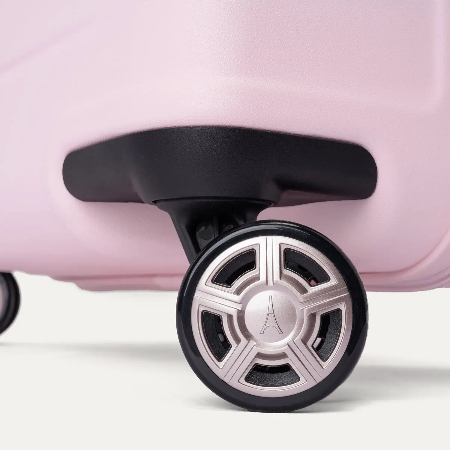 Close-up of the dual spinner wheels on the Travelpro Platinum Elite Next Gen Powder Pink Suitcase, featuring self-aligning MagnaTrac technology, a black rubber tire, and a metallic silver hub with an Eiffel Tower logo against a clean off-white background.