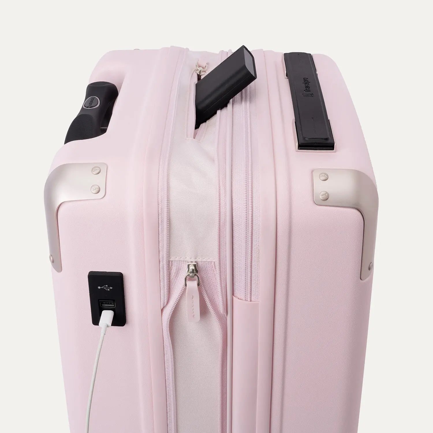Close-up view of theTravelpro Platinum Elite Next Gen Powder Pink Suitcase, featuring an integrated USB charging port with a white cable plugged in, a side pocket, and a black handle against an off-white background.