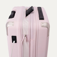 Close-up view of theTravelpro Platinum Elite Next Gen Powder Pink Suitcase, featuring an integrated USB charging port with a white cable plugged in, a side pocket, and a black handle against an off-white background.