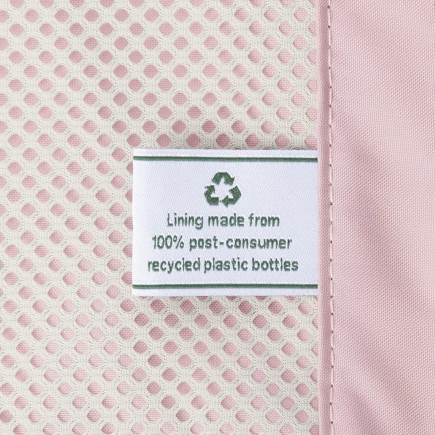 Close-up detail of the ECOFAB lining inside the Travelpro Platinum Elite Next Gen Powder Pink Suitcase, featuring a white fabric label that reads "Lining made from 100% post-consumer recycled plastic bottles" with a green recycling symbol against the pink mesh interior.