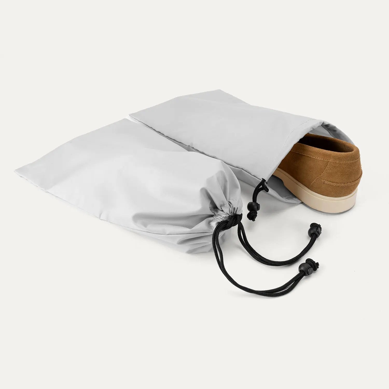 Close-up of the two removable grey drawstring shoe bags included with the Travelpro Platinum Elite Carry-On Hardside Spinner, showing a brown shoe partially inserted to demonstrate organizational use.
