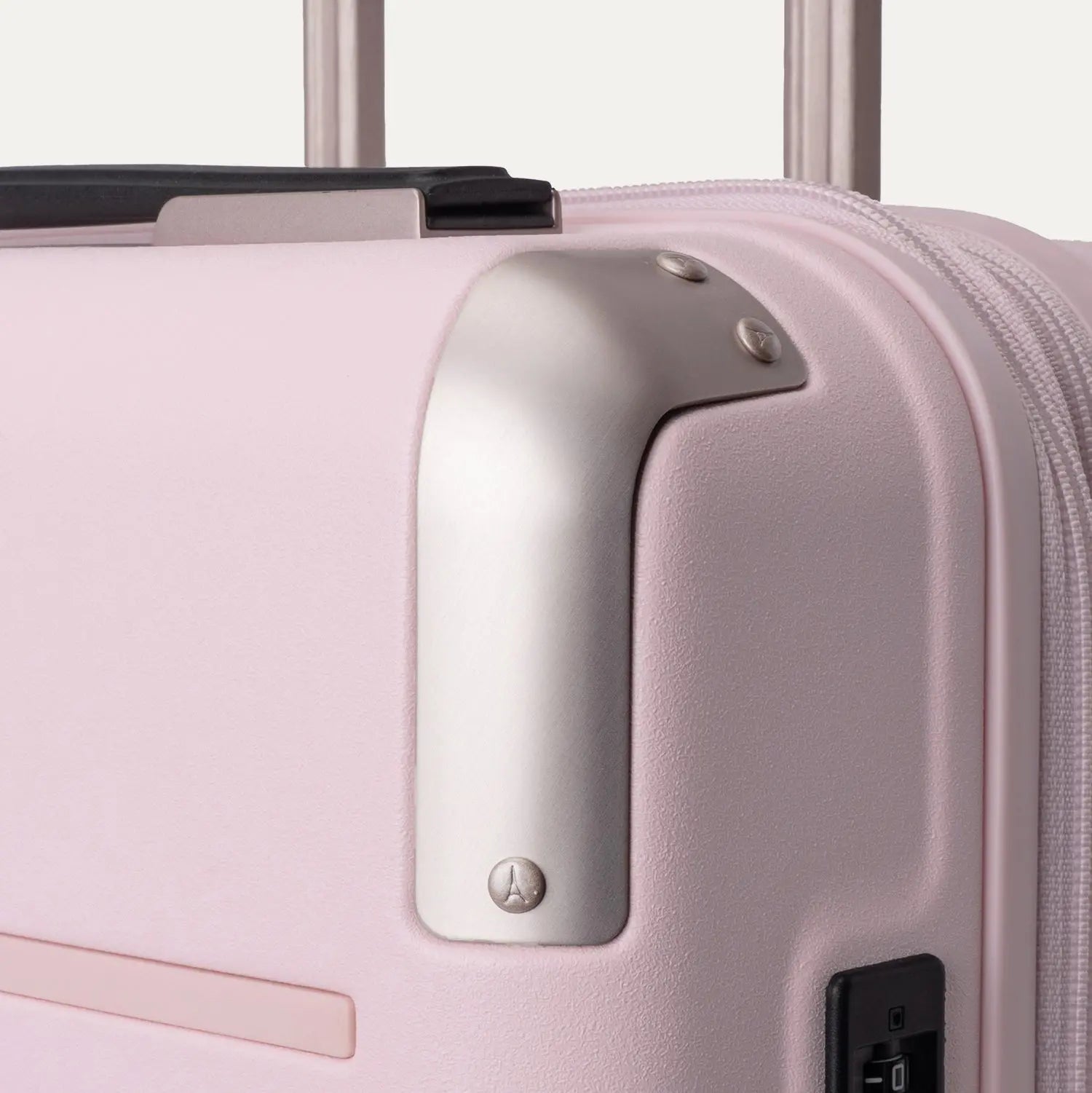 Close-up view of the light pink Travelpro Platinum Elite Next Gen Powder Pink Suitcase, highlighting the metallic corner guard, top carry handle, zipper, and telescoping handle against an off-white background.