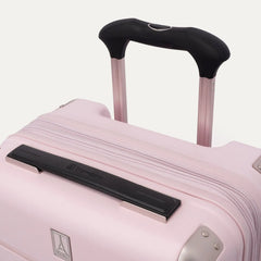 Close-up of the light pink Travelpro Platinum Elite Next Gen Powder Pink Suitcase, featuring an extended black ProGrip telescoping handle, a black top carry handle, metallic corner guards, and the Travelpro logo badge against a clean off-white background.