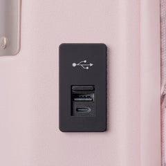 Close-up view of the black rectangular USB charging port panel mounted on the light pink Travelpro Platinum Elite Next Gen Powder Pink Suitcase, featuring a USB symbol and charging ports against an off-white background.