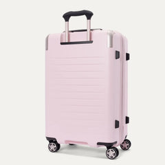 Three-quarter rear view of the Travelpro Platinum Elite Medium Check-In Hardside Spinner in Powder Pink, featuring a durable polycarbonate shell with polished aluminum corner armor, an extended telescopic handle, and multi-directional wheels against a clean off-white background.