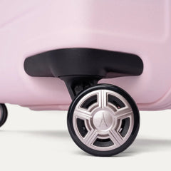Close-up of the dual spinner wheels on the Travelpro Platinum Elite Medium Check-In Hardside Spinner in Powder Pink, featuring self-aligning MagnaTrac® technology, a black rubber tire, and a metallic silver hub with an Eiffel Tower logo against a clean off-white background.