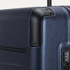 Close-up detail of the Travelpro Platinum Elite Large Check-In Hardside Spinner in Aviator Navy, showing the integrated TSA-approved combination lock and protective polished aluminum corner armor.